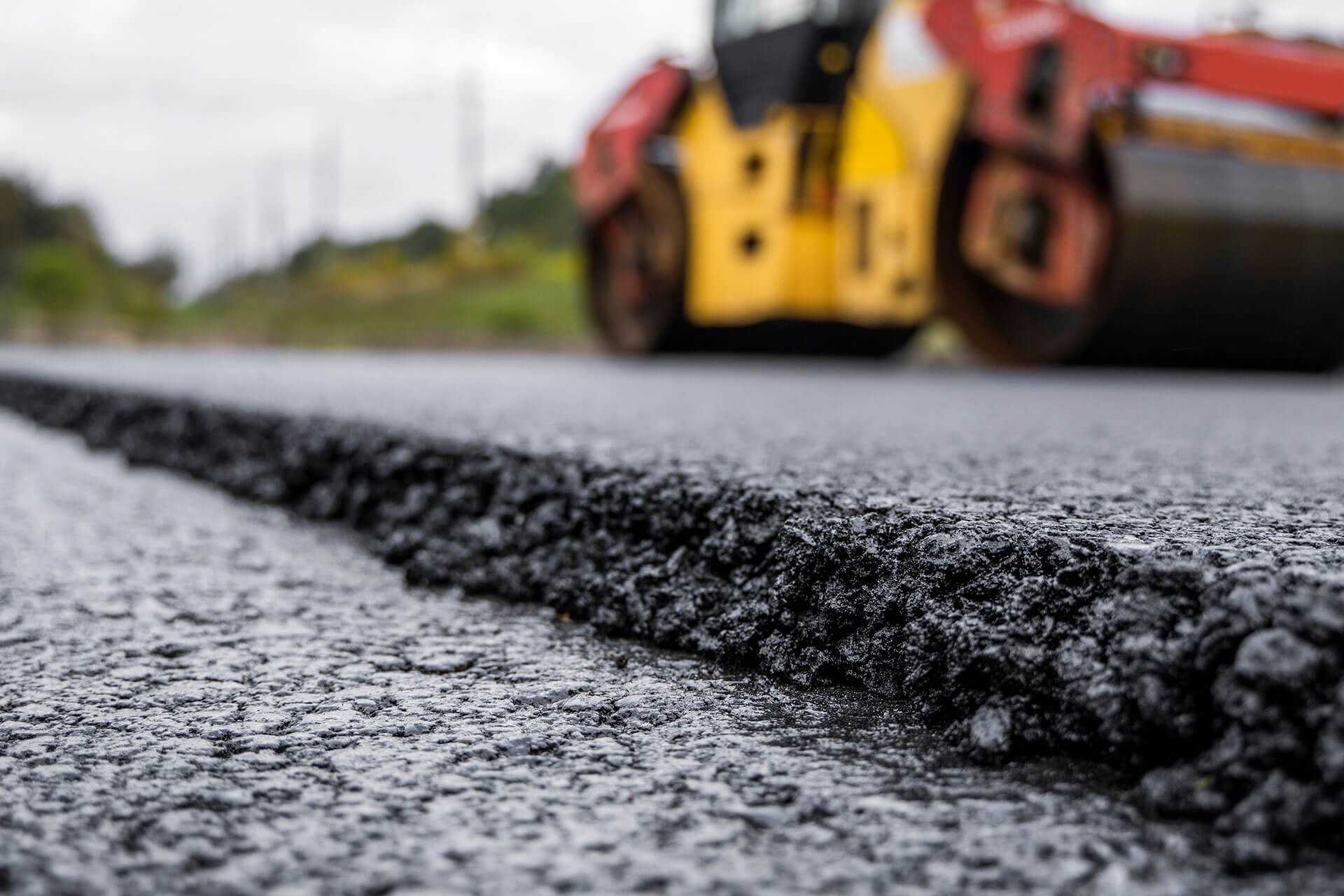 Im Vordergrund Asphaltkante und Hintergrund Baumaschine